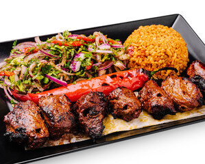Grilled meat platter with rice and fresh salad served on a black plate