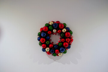 Christmas wreath composed of Christmas balls of different colors on a white wall.