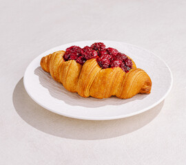 Fresh raspberry croissant served on a white plate in natural light