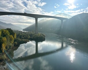 Sunlit bridge reflected in the hazy river Douro flowing through the mountain valley, Peso da Régua, Vila Real, Portugal, November 2024