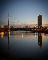 Fototapeta premium Emajõgi riverside view at twilight with illuminated Turu bridge and Tigutorn skyscraper, Tartu, Tartumaa, Estonia, November 2020