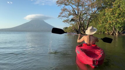 A mature woman paddles her kayak through the calm waters of Lake Nicaragua, surrounded by nature and Concepcion volcano in the distance.