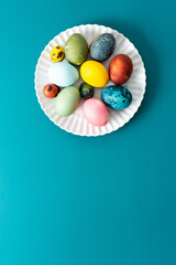 A beautiful assortment of Easter eggs in various colors and patterns is displayed on a round white plate against a bright blue background, perfect for holiday festivities