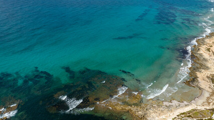 Obraz premium Aerial view of the rocky coastline overlooking the sea. The water ranges from turquoise to blue and is very clean and transparent. Located in Sicily, Italy. Sunny summer day.