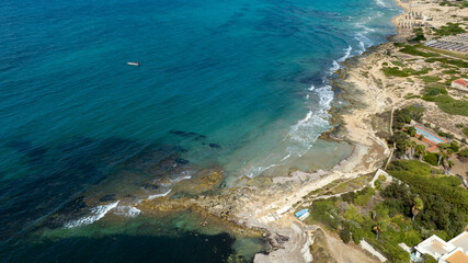 Aerial view of the rocky coastline overlooking the sea. The water ranges from turquoise to blue and is very clean and transparent. Located in Sicily, Italy. Sunny summer day.