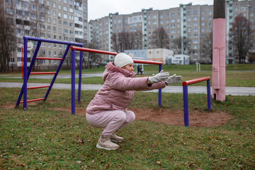 Pensioner doing squats exercises at stadium. Senior woman practice sports outdoors. Retiree healthy lifestyle, outdoor physical activity in city.