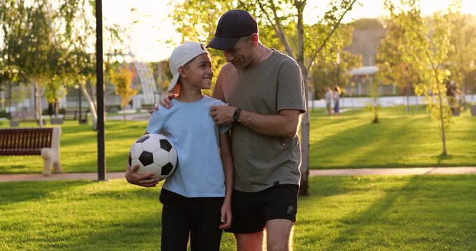 Adult and child boy walk in park with soccer ball at sunset. Father and son enjoy outdoor time in warm summer. Outdoor walk shows happy mood and positive connection. supports family sport concept.