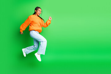 Young woman jumping in a bright orange sweater against a green screen for fashion fitness lifestyle and joyful moment