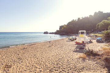 Golden-hour beach scene featuring a white lifeguard tower, colorful kayaks, and people swimming near rocky cliffs.