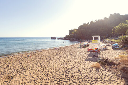 Golden-hour beach scene featuring a white lifeguard tower, colorful kayaks, and people swimming near rocky cliffs.