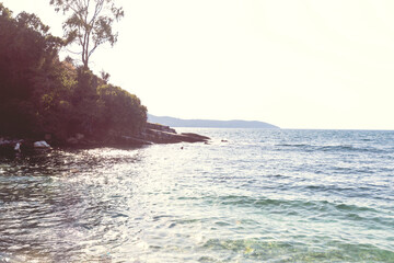Calm turquoise waters shimmer under golden sunlight along a secluded rocky shore