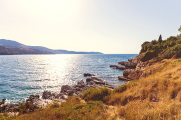 Serene rocky coastline with sunlit sea and distant mountains