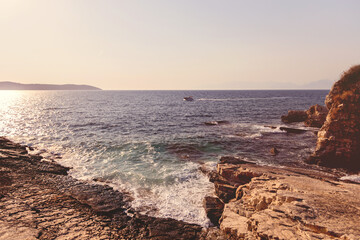 Small boat driving past rocky coastline at sunset golden hour