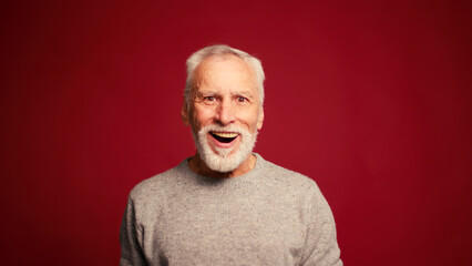Obraz premium Stylish excite mature bearded man with open mouth looking at camera isolated on red background
