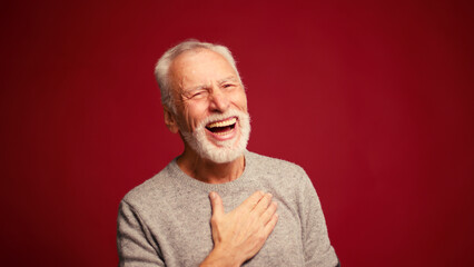 Portrait of smiling happy elderly man laughing looking at camera isolated on red background