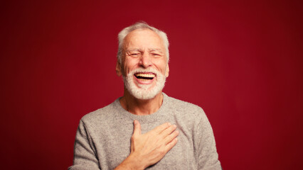 Portrait of smiling happy elderly man laughing looking at camera isolated on red background