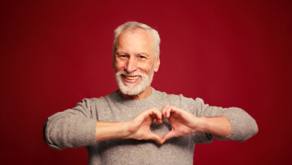 Smiling, handsome senior man ending air kiss, looking at camera isolated on red background