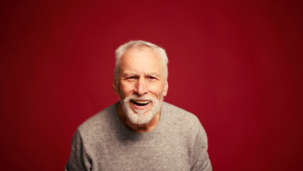 Obraz premium Happy, handsome senior bearded man looking at camera isolated on red background