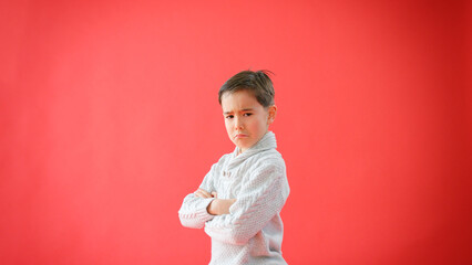 Portrait Of Serious Young Boy With Folded Arms Against Red Studio Background
