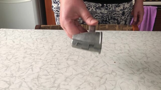 A close-up shot of a hand holding up a metallic nutcracker tool over a kitchen counter. The scene highlights food preparation, cracking nuts, and kitchen equipment.