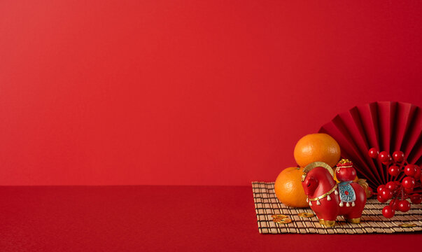 Side view of a red festive setting featuring Chinese New Year lanterns, oranges, and a decorative horse statue on a bamboo mat, symbolizing luck, prosperity, and festive greetings