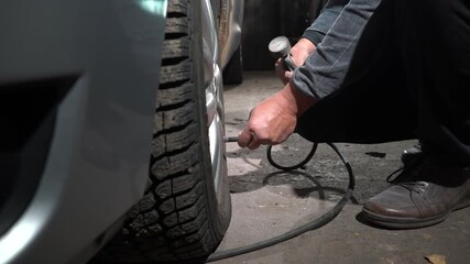 A person is adjusting the tire pressure of a vehicle in a dimly lit garage. The individual uses an air pump to inflate the tires properly. Safety is prioritized.
