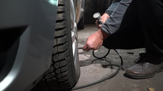 A person is adjusting the tire pressure of a vehicle in a dimly lit garage. The individual uses an air pump to inflate the tires properly. Safety is prioritized.