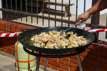 Paella pan, man's hand frying chicken to then cook all the other ingredients and prepare the typical paella