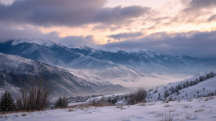 Snowy mountain range landscape with clouds and fog covering the valley in a winter scene at dusk or dawn
