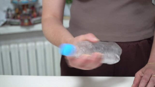In a bright kitchen, a man shakes a plastic water bottle to stir the contents and quickly produce ice-cold water.