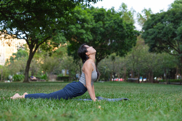 Woman practicing upward dog yoga pose at green park