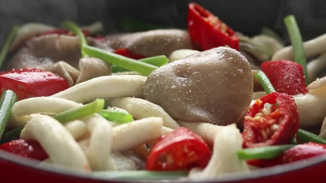 Stir-frying grey indian oyster or phoenix mushrooms with red chilli spur pepper in a hot pan. Close-up shot	