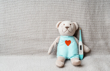 Toy bear with thermometer lays covered with baby blanket- top view. Children Healthcare concept photo.