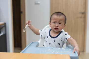 Baby eating with spoon making messy food at home