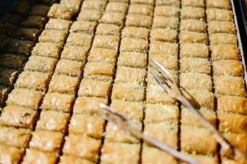 Close-up, high-angle view of golden syrup-soaked Baklava-style pistachio rolls cut into uniform pieces, with two silver serving forks