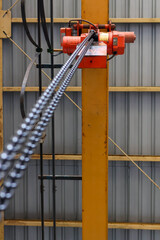 Naklejka premium Low angle view Industrial red chain hoist (overhead crane) mounted on a yellow vertical steel beam in a factory or warehouse, emphasizing heavy lifting equipment and industrial construction.