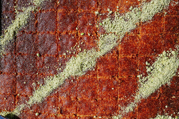 Extreme close-up of Knafeh syrup-soaked Middle Eastern dessert cut into squares and heavily garnished with a diagonal pattern of crushed pistachios