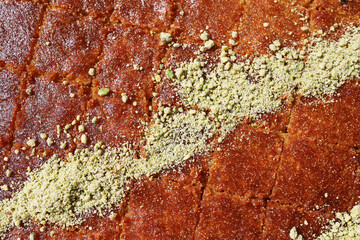Extreme close-up of Knafeh syrup-soaked Middle Eastern dessert cut into squares and heavily garnished with a diagonal pattern of crushed pistachios