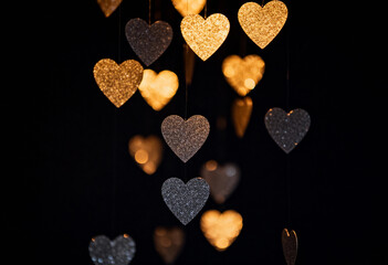 Hanging golden and silver glitter hearts against a dark background for Valentines Day holiday poster flyer greeting card