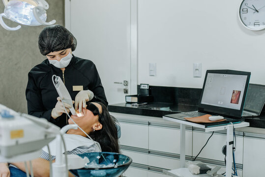 Dentist performing a digital teeth scan with an intraoral scanner while the patient lies in the dental chair.