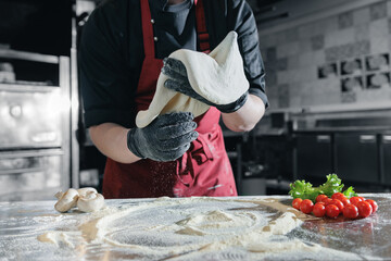 Male chef pizzamaker preparing pizza flying thin dough in rustic pizzeria kitchen