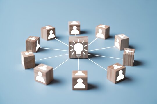 A bright idea is shared among a group of people, represented by wooden blocks with light bulb and person icons on a blue background