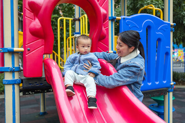 Mother taking her baby to play slide in park