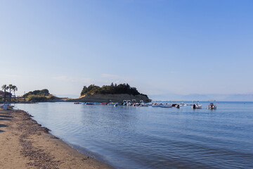 Tropical beach with boats and island view under clear blue sky in serene coastal setting.
