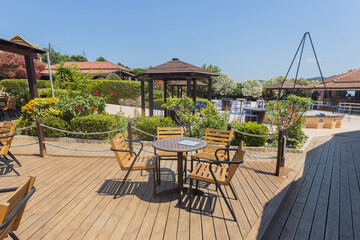 Wooden deck with table and chairs overlooking pool and gazebos in sunny resort garden.