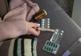 Woman holding thermometer with medicine blister packs