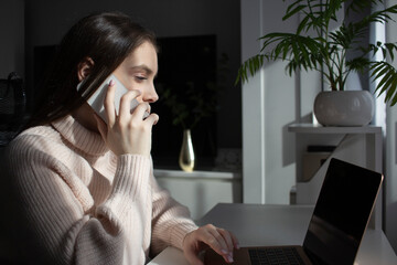 Woman talking on phone while working on laptop at home