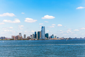 Jersey City skyline across the Hudson River on a sunny day with modern skyscrapers and blue water.
