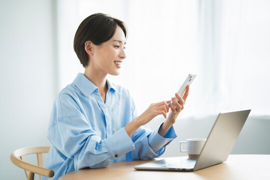 リビングで椅子に座り、パソコンを開いて携帯電話を見る日本人女性