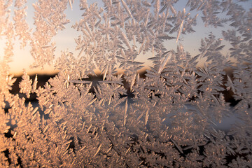 Delicate frost patterns on a windowpane with warm sunrise light filtering through